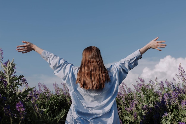 Mujer irreconocible con los brazos extendidos de pie solo campo de flores púrpuras en frente del cielo