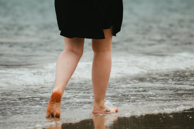 Mujer irreconocible caminando por la playa en un día nublado