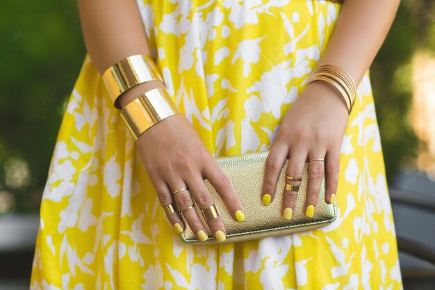 Mujer irreconocible con cartera en sus manos. Lady`s manos con anillos y accesorios. Chica en vestido amarillo