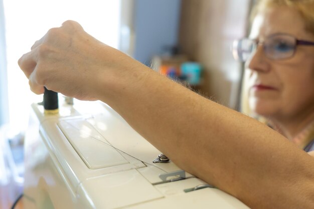 Mujer irreconocible colocando carrete de hilo en la máquina de coser
