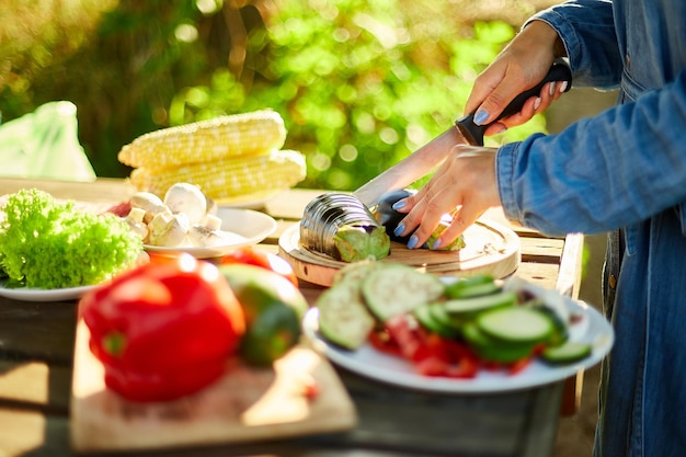 Mujer irreconocible cortando verduras frescas de berenjena en una tabla de madera durante la barbacoa de fin de semana en el patio al aire libre preparándose para asar comida de picnic familiar de verano en la naturaleza