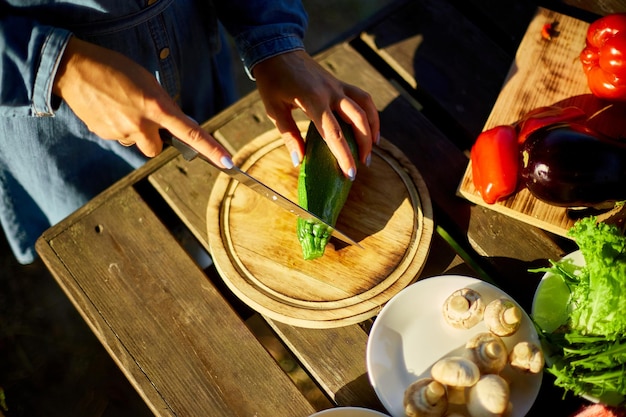 Mujer irreconocible cortando verduras frescas de calabacín en tablero de madera