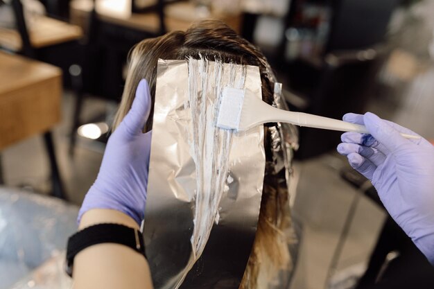 Foto mujer irreconocible estilista colorista sostenga un mechón de cabello largo sobre papel de aluminio aplicando tinte para el cabello con br