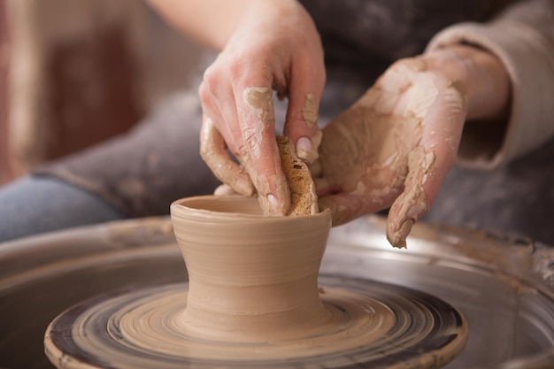 Mujer irreconocible haciendo cerámica, usando un torno de alfarero para dar forma a una taza de arcilla