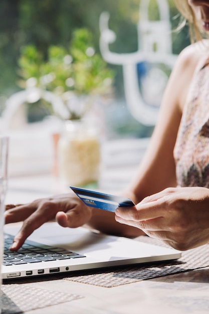 Mujer irreconocible haciendo compras en línea con tarjeta de crédito usando una computadora portátil en un café