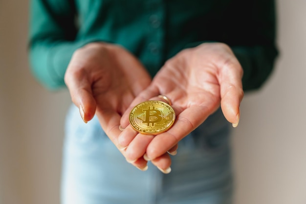 Mujer irreconocible haciendo gesto de dar una moneda bitcoin dorada. Ahorro seguro en dinero virtual