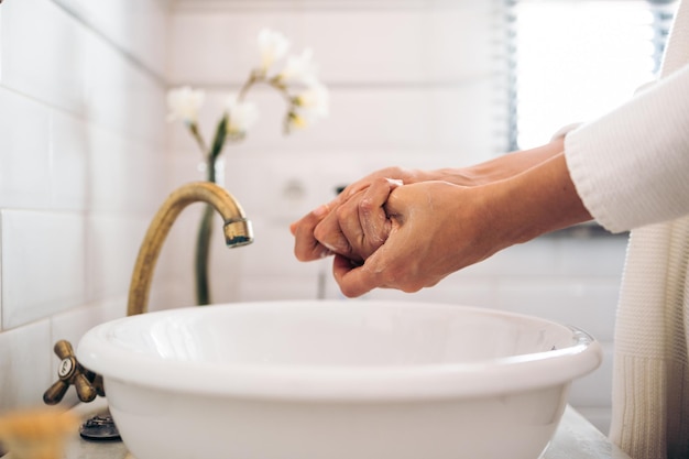 Mujer irreconocible lavándose las manos con jabón en un baño antiguo