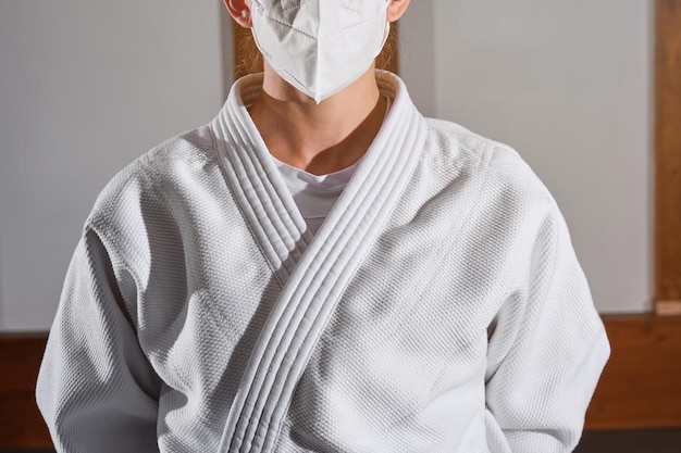 Foto mujer irreconocible con mascarilla médica y kimono parada en una habitación luminosa durante una situación pandémica