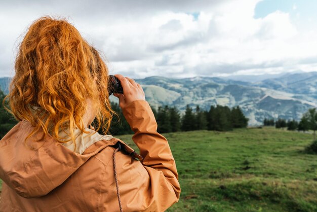 Foto mujer irreconocible mirando a través de binoculares en un paisaje verde con montañas en el fondo