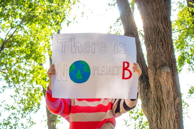 Mujer irreconocible en la naturaleza con pancarta de cambio climático