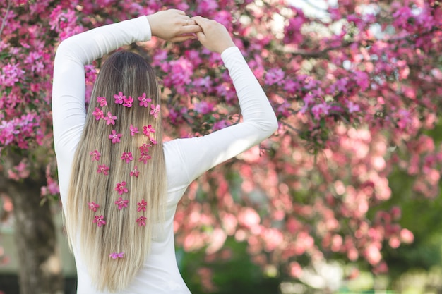 Mujer irreconocible que se coloca detrás de la cámara con el pelo largo y rubio con flores en el pelo. Mujer sobre fondo de primavera. Dama al aire libre.