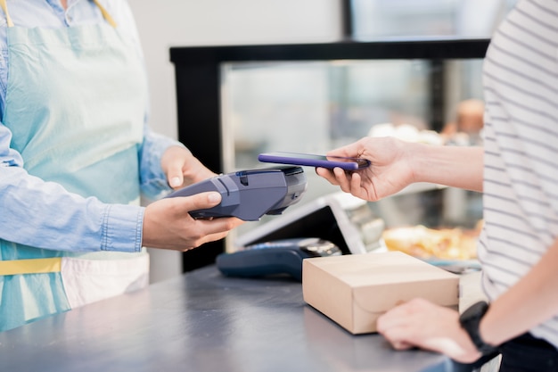 Mujer irreconocible que paga por teléfono inteligente en la tienda