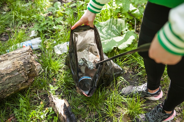 Mujer irreconocible recogiendo basura en el bosque después de un picnic