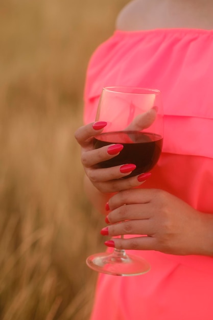 Mujer irreconocible sosteniendo una copa de vino tinto de pie en la naturaleza al atardecer Parte del cuerpo de la mujer con un vestido brillante con alcohol en el campo