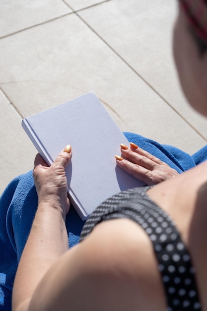 Foto mujer irreconocible sosteniendo una revista en blanco para un diseño de maqueta sentada junto a la piscina