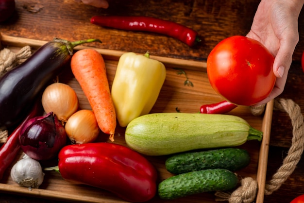 Una mujer irreconocible sostiene un tomate sobre un fondo de diferentes vegetales El concepto de vegetarianismo alimentario saludable