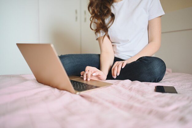 Mujer irreconocible trabajando en una computadora portátil y teléfono en la cama