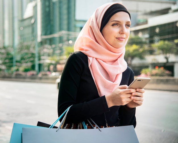 Mujer islámica con bolsas de la compra y la celebración de teléfono móvil