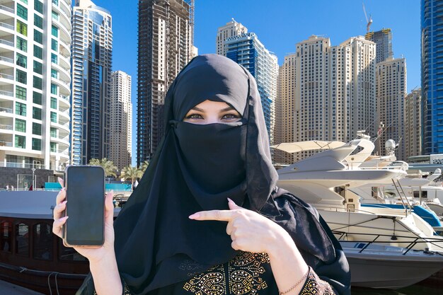 Foto mujer islámica muestra su dedo en su teléfono en el contexto de la ciudad.