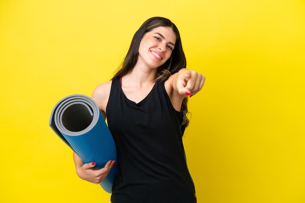 Mujer italiana deportiva que va a clases de yoga aislada de fondo amarillo apuntando al frente con expresión feliz