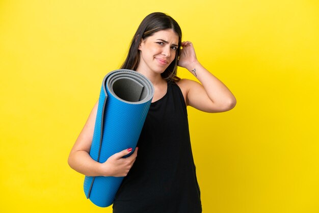 Mujer italiana deportiva que va a clases de yoga aislada de fondo amarillo con dudas