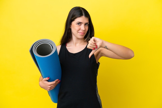 Mujer italiana deportiva yendo a clases de yoga aislada de fondo amarillo mostrando el pulgar hacia abajo con expresión negativa
