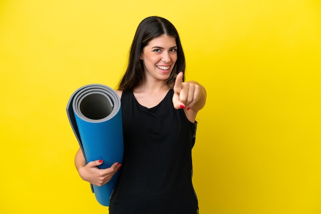 Mujer italiana deportiva yendo a clases de yoga aislada de fondo amarillo sorprendida y apuntando al frente