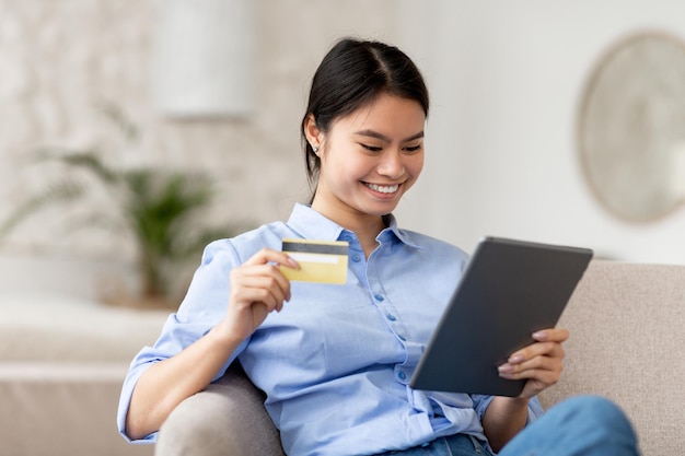 Mujer japonesa alegre comprando en línea usando almohadilla y tarjeta de crédito