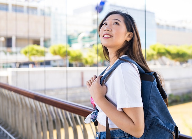 Mujer japonesa con una mochila al aire libre, mirando hacia arriba