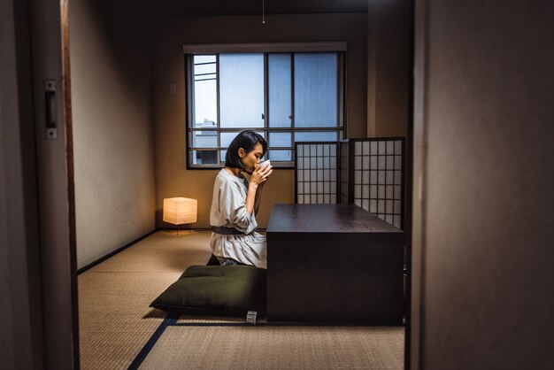 Mujer japonesa se sienta en casa y bebe té