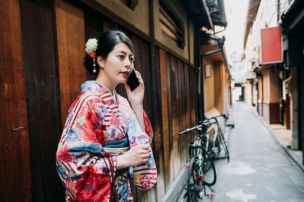 mujer japonesa con vestido de kimono hablando por celular. concepto de tecnología de tela tradicional de los jóvenes. hermosa mujer local lista para unirse al festival de verano de pie en el camino con bicicleta en segundo plano