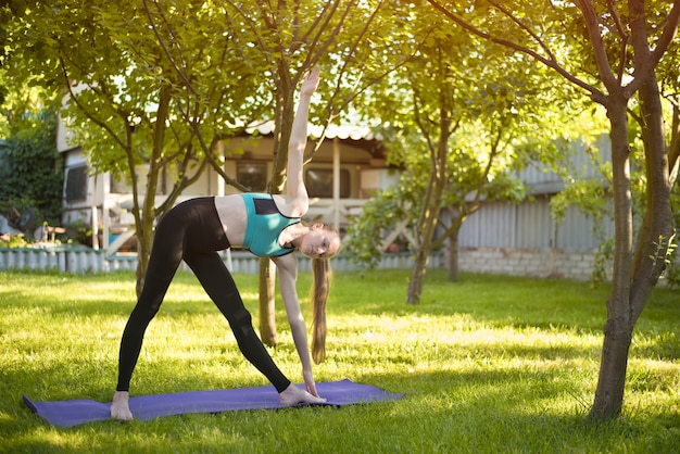 Mujer en el jardín practica yoga. Pose del triángulo. Mañana de verano.