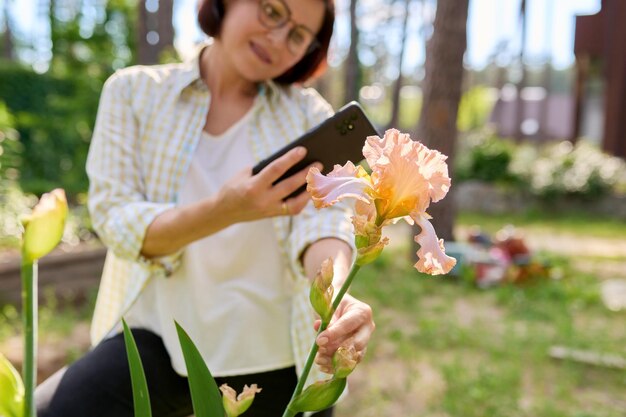 Mujer en el jardín de primavera disfrutando de la belleza de las flores de iris tomando fotos de iris con un teléfono inteligente