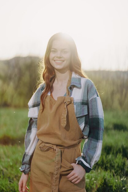 Foto una mujer jardinera en un delantal se encuentra en un campo de hierba verde al aire libre sonriendo en un día de verano en una puesta de sol foto de alta calidad