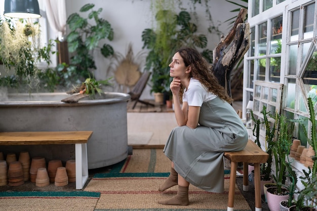 Mujer jardinera descansando después del trabajo en una tienda de flores o en un invernadero soñando y mirando por la ventana