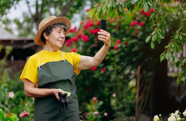 Mujer jardinera senior en un sombrero trabajando en su jardín y habla por teléfono El concepto de jardinería creciendo y cuidando flores y plantas