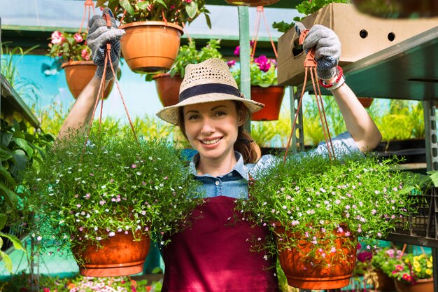 Mujer jardinera con sombrero y guantes trabaja con flores en el invernadero