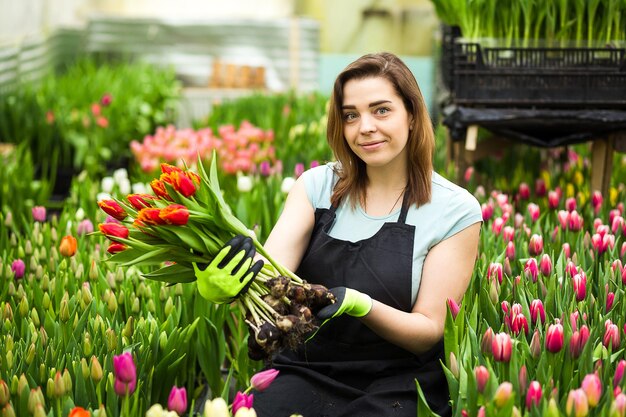 Mujer jardinero floristería sosteniendo un ramo de flores de pie en un invernadero donde se cultivan los tulipanesJardinero sonriente sosteniendo tulipanes con bulbosPrimavera un montón de concepto de flores
