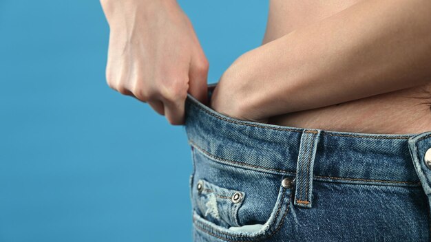 Una mujer en jeans de gran tamaño sobre fondo azul con espacio para copiar Pérdida de peso y alimentación saludable