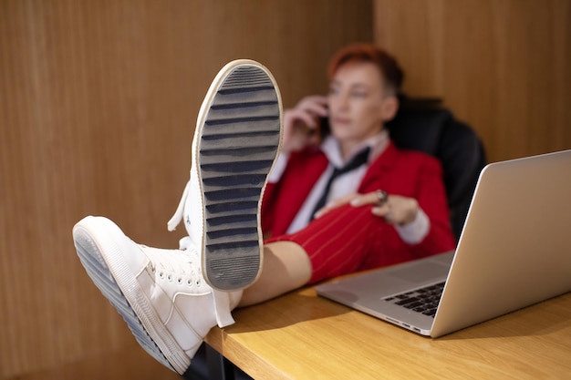 Foto mujer jefe descansando en el trabajo mujer de negocios usando el teléfono y los pies en la mesa