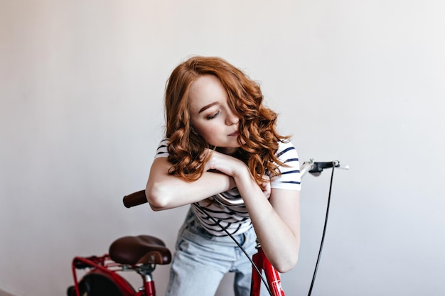 Mujer de jengibre de buen aspecto posando con bicicleta sobre fondo blanco Foto interior de una dama maravillosa de pie en el estudio con bicicleta