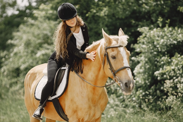 Mujer jinete montando su caballo en un rancho. La mujer tiene cabello largo y ropa negra. Ecuestre femenina tocando su caballo marrón.