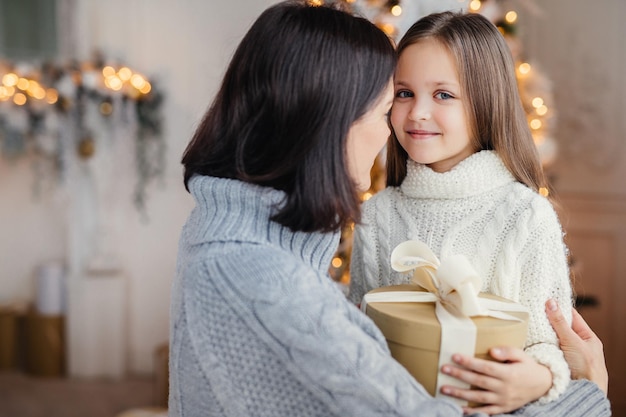 La mujer joven abraza a su hijito y le da un regalo de Año Nuevo orgullosa de tener una hija tan hermosa e inteligente Niño feliz pasa tiempo con su madre Infancia y vacaciones