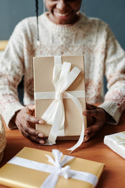 Mujer joven abriendo una caja de regalos junto a la mesa.