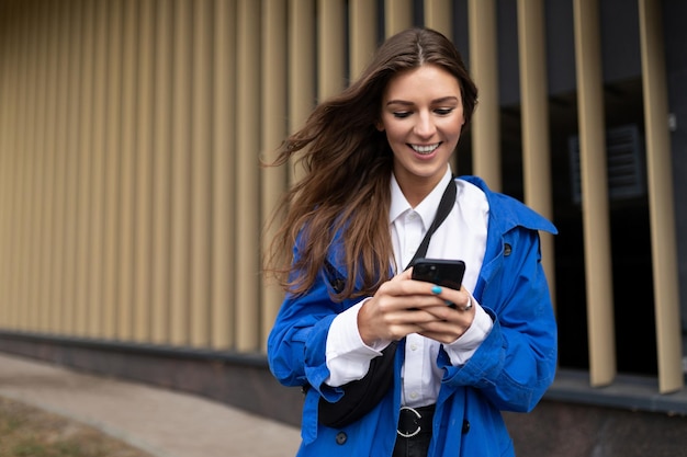 Una mujer joven con un abrigo azul de otoño con una sonrisa en la cara tiene prisa por hacer negocios mirando un
