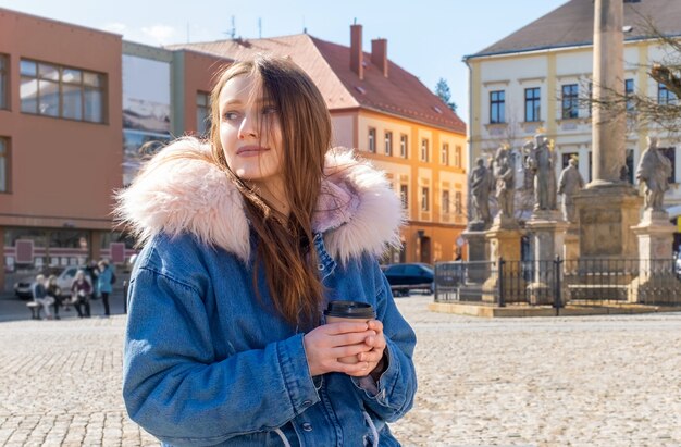 Mujer joven con un abrigo en la calle con un café