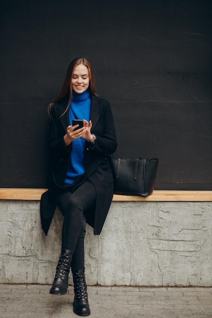 Mujer joven, en, abrigo negro, utilizar, teléfono