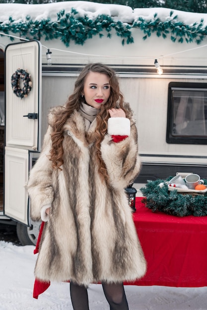 Mujer joven en abrigo de piel con caja de regalo en el campamento de invierno preparándose para el nuevo año