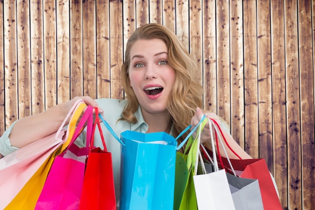 Mujer joven abrumada con bolsas de compras contra tablones de madera