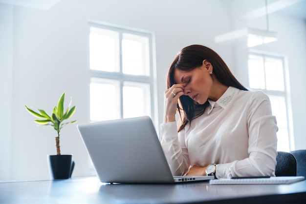 Mujer joven aburrida en la oficina trabajando con una computadora portátil